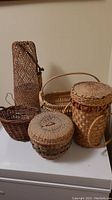 Photo showing five different handwoven baskets made of natural fibers varying in size and shape on a white surface.