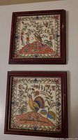 Photo showing two framed ceramic tiles mounted on wall featuring colorful birds and floral designs.