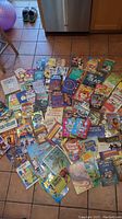 Full overview of collection of about 48 children's books spread on floor showing a wide variety of titles and colorful covers.