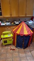 Wood toy kitchen, kids circus tent, and wood pull-along dog toy on tiled kitchen floor.