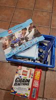 Photo showing a blue plastic storage box with LEGO Education instruction manuals, including a cover marked 9686 and a Chain Reactions booklet.