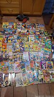 Image showing a wide array of comic books spread out on the floor, featuring titles such as Richie Rich, Mickey Mouse, Tom & Jerry, and various Marvel and DC comics.