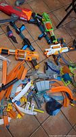 Multiple Nerf toy guns, including orange, green, and white models, and various Hot Wheels track pieces on floor