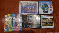 Top-down photo showing all four puzzles and the Big Bang Theory game box arranged on wooden floor.