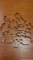 Top view of all 10 cookie cutters arranged on a wooden surface, showing pairs of small and large shapes including stars, flowers, trees, angels, gingerbread men, birds, and ducks.