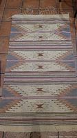 Full view of woven rug laid flat on tiled floor showing pattern and fringes.