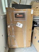 Photo of the fireplace box with taped cardboard and a printed image showing the electric fireplace design with flames.
