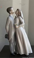 Side view of the Lladró wedding couple figurine showing the bride and groom leaning close, bride holding bouquet, on a black base.
