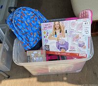 Large tote bin showing the collection of items inside including backpack, nail art kit, roller skates, figurines, and robot dog.