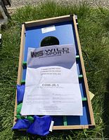 Top view of game board with instruction manual showing brand and model COM-JR-1, includes blue and green bean bags arranged on board.