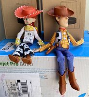 Woody and Jessie wind-up dolls sitting on box, showing full front and side views and detailed clothing