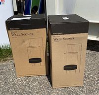 Two cardboard boxes containing the Mason wall sconces from World Market. Each box shows line art depiction of the sconce and product information.