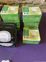 Four green boxes of 4 inch slim LED panel pot lights stacked on top of each other and black boxes of slim LED fixtures beside them.