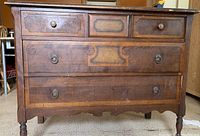Front view of antique wooden dresser showing three drawers, two small ones with wooden knobs on top and two larger ones with metal ring pulls below, with carved decorative details.