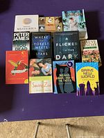 Photo showing 12 books arranged on purple surface to show various titles and covers for condition and identification.