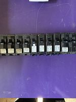 Ten single pole 15 Amp circuit breakers arranged horizontally on purple surface, showing brand labels and amperage rating.