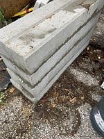 Stack of eight gray concrete curb stones on outdoor ground.