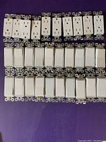 Photo showing rows of Decora style white electrical outlets and switches laid out on surface.
