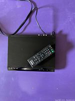 Top view of the black Sony DVD player with the remote placed on top, showing cables connected at the back.