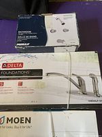 Photo showing the packaging of Peerless 4-piece shower faucet kit, Delta Foundations kitchen faucet, and Moen box.