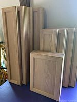 Stack of pre-finished solid oak cabinet door faces showing wood grain and panel design.
