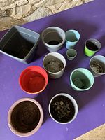 Top-down view of 11 used planting pots in various materials and colors placed on a purple surface.