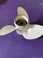 Top-down view of white 3-blade boat propeller showing blade shape and central hub