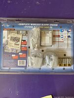 Photo of wireless alarm system packaging showing accessories including white plastic components, batteries, and mounting hardware.