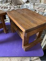 Close-up side view of one wooden end table showing plank top and leg construction