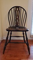 Front view of an antique Windsor wood side chair, showing the curved spindle back and turned legs.