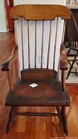 Front view of the antique wooden rocking chair showing the spindle backrest, curved top rail, armrests, and seat with visible wear.