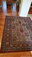 Top down angled view of detailed patterned rug on wooden floor, showing multicolor traditional Persian-inspired design with brown, cream, and dark red tones.