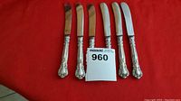 Six spreader knives laid side by side on red fabric