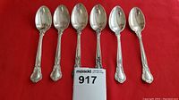 Six Birks sterling silver teaspoons arranged in a row on a red fabric background showing their shape and ornate handles.