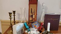 Brass candlesticks, glass decanter, vase, basket with small liquor bottles and snacks, Diners journal, and candles arranged on table.