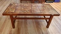 Front view of rectangular wooden coffee table with tile inset top on wood floor.