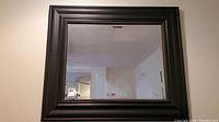 Full front view of the rectangular framed mirror hanging on a wall, showing reflective beveled glass and dark wide frame with beaded border detail.