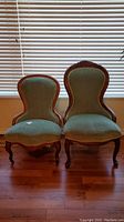 Front view of two vintage Victorian style upholstered chairs, gentleman's and lady's, placed side by side on wooden floor.