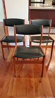 Three teak dining chairs together viewed from front, hardwood floor and kitchen background