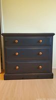 Front view of navy blue three-drawer dresser showing natural wood knobs