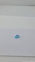 Natural blue topaz gemstone displayed on a white surface showing its pear shape and clarity.