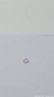 Clear image of a small cushion cut pink sapphire gemstone on a plain white background showing the gemstone's color and faceting details.