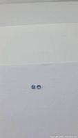 Photo showing two small round diamond cut tanzanite stones placed side by side on white background with slight blue to purple coloration.