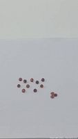 Photo of 14 round cut orange red garnet gemstones scattered on a white background, showing their rare color and clarity.