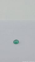 Oval cut green emerald gemstone shown from top angle on white background.