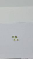Four square princess cut apple green Peridot gemstones on a white surface, clearly showing their size and bright color.