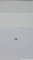 Photo showing a small emerald cut bright apple green peridot gemstone on a plain white background for clear visibility of size and color.