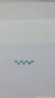 Eight small baguette cut green emerald gemstones laid out on a white surface, showing their rectangular shape and clarity.