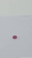 Single oval cut ruby gemstone with deep pink-red color on a plain background.