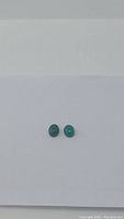 Two small natural green onyx oval cabochon gemstones placed side by side on a white background, showing their size and color.